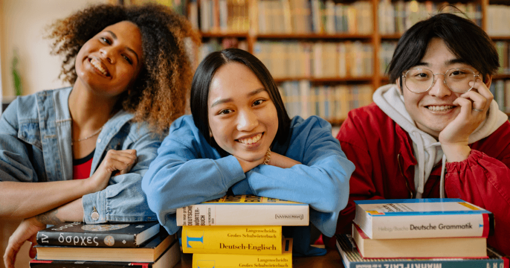 A group of college students smiling and leaning on their books to represent Education Grants